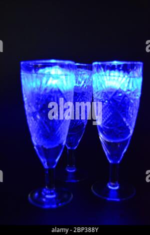 Crystal champagne glasses with carvings in the form of snowflakes are located on a black matte background. Bright multicolor doidic glowing ice cubes Stock Photo