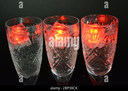 Crystal champagne glasses with carvings in the form of snowflakes are located on a black matte background. Bright multicolor doidic glowing ice cubes Stock Photo