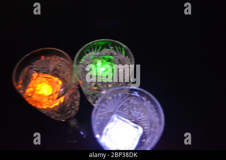 Crystal champagne glasses with carvings in the form of snowflakes are located on a black matte background. Bright multicolor doidic glowing ice cubes Stock Photo