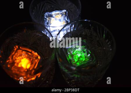 Crystal champagne glasses with carvings in the form of snowflakes are located on a black matte background. Bright multicolor doidic glowing ice cubes Stock Photo