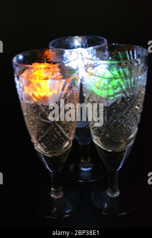 Crystal champagne glasses with carvings in the form of snowflakes are located on a black matte background. Bright multicolor doidic glowing ice cubes Stock Photo