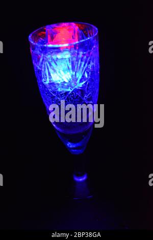 Crystal champagne glasses with carvings in the form of snowflakes are located on a black matte background. Bright multicolor doidic glowing ice cubes Stock Photo