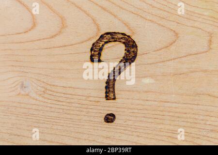 question mark drawn with handheld woodburner on bright flat wooden surface Stock Photo