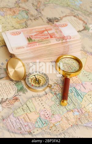 A compass with a bundle of big money and a magnifying glass are on the map Stock Photo