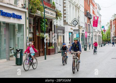 Family cycling through deserted Grafton Street in Dublin Ireland as businesses and shops remain closed and footfall plummets due to Covid-19 lockdown Stock Photo