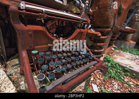 Classic rusty typewriter sits broken and discarded on ground exposed to elements a relic of previous times. Part of an art installation Cathedral of J Stock Photo