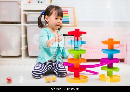 toddler girl play marble run game at gome agianst white background Stock Photo