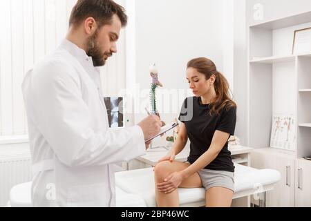 Male doctor examining female patient suffering from knee pain. Medical exam. Chiropractic, osteopathy, post traumatic rehabilitation, sport physical Stock Photo