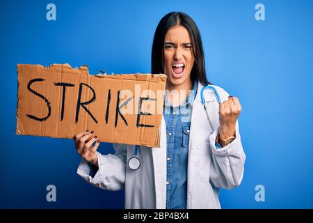 Young doctor woman wearing stethoscope holding cardboard banner protesting in strike annoyed and frustrated shouting with anger, crazy and yelling wit Stock Photo