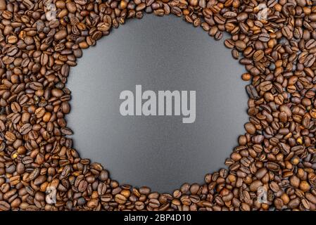 Background made of fresh roasted coffee beans lying flat on a black background with copy space in the shape of a circle. Stock Photo