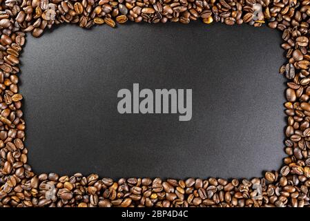 Background made of fresh roasted coffee beans lying flat on a black background with copy space in the shape of a rectangle. Stock Photo