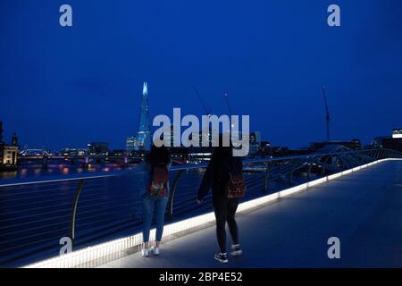 London, UK, 17 May 2020: People walk and cycle across the Milemmium Bridge as the top of the Shard is illuminated blue and Tate Modern carries signage saying 'Thank you key workers' to honour NHS staff and other care workers and frontline key workers. Anna Watson/Alamy Live News Stock Photo
