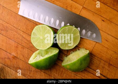 Juiced limes cut in half on a wooden cutting board with a knife; squeezed or reamed for juicing. Stock Photo