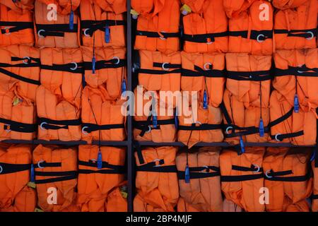 Rows of bright orange life jackets with black straps and blue whistles stacked up against a wall on a tourist boat on the Panama Canal.  Background Stock Photo