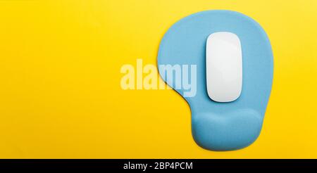 Top view flat lay of blue pad or mousepad with wireless white computer mouse modern design isolated on a yellow background and copy space Stock Photo