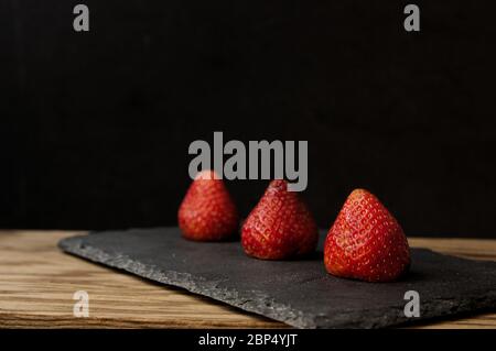 Three strawberries on a black slate and dark background illuminated in the dark food mode Stock Photo
