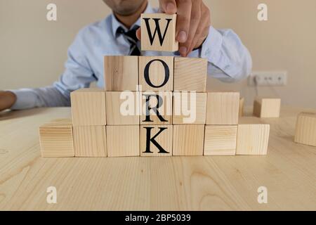 It writes the word work on wooden blocks. The man in the suit puts the block on top. Stock Photo