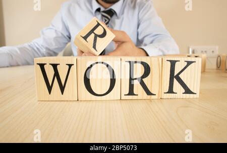 It writes the word work on wooden blocks. The man in the suit puts the block on top. Stock Photo