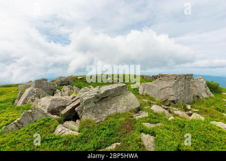 huge stones in valley on top of mountain ridge. mountain summer landscape. meadow with huge stones among the grass on top of the hillside near the pea Stock Photo