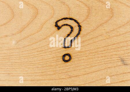 question mark drawn with handheld woodburner on flat wooden surface Stock Photo