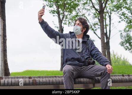 Young tourist with surgical mask in video call with his smartphone, photographer with health care mask in urban exploration take a selfie, sitting on Stock Photo
