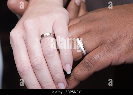 Close up detail shot of Interracial couple holding hands showing modest wedding rings. Stock Photo
