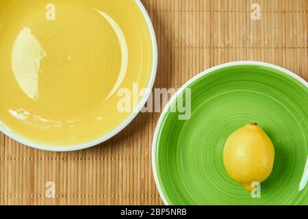 color still life - lemon on a green plate next to a yellow empty plate on a cane tablecloth Stock Photo