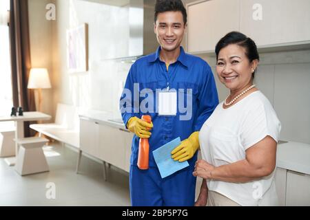 Portrait of happy senior Vietnamese woman and cleaning service worker holding detergent with cellulose sponge Stock Photo