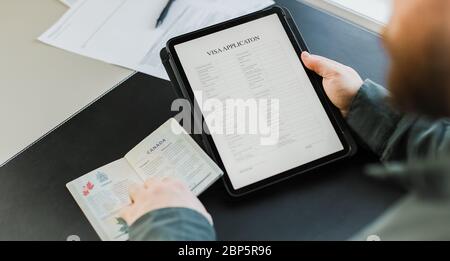 Bearded man applying for visa on tablet and holding passport, Canada. Stock Photo