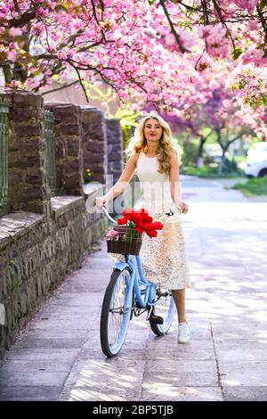 Spring style travel. retro woman sell tulip flower bouquet. girl under sakura with vintage bicycle. spring beauty and fashion. cherry tree pink blossom. perfect smell. perfume spa and allergic. Stock Photo