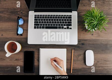 Woman watching webinar on laptop and writing important detail in textbook Stock Photo