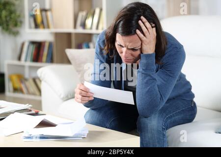 Sad adult woman checking receipts sitting in the sofa in the livingroom at home Stock Photo