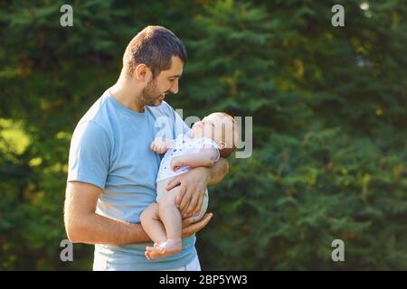 Father's day. Caring father holds the baby in his arms in the park Stock Photo