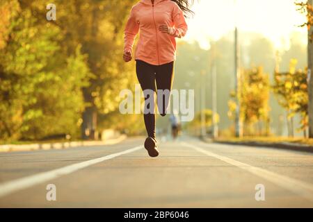 A girl in sportswear runs on the road in the autumn park.