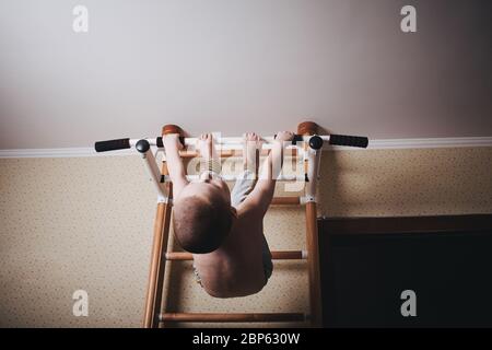 Home workout. The boy hangs head down on the horizontal bar. Stock Photo