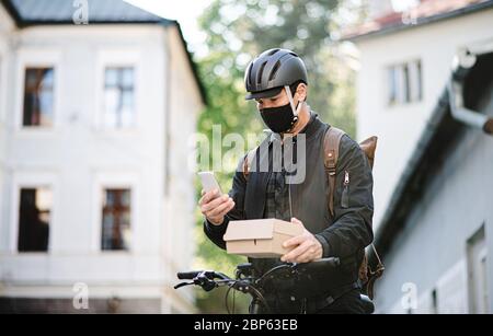 Delivery man courier with face mask and bicycle using smartphone in town. Stock Photo