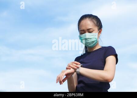 young asian woman in medical protective mask doing setting smart watch application before exercise in the morning.working out outdoor. Concept of heal Stock Photo