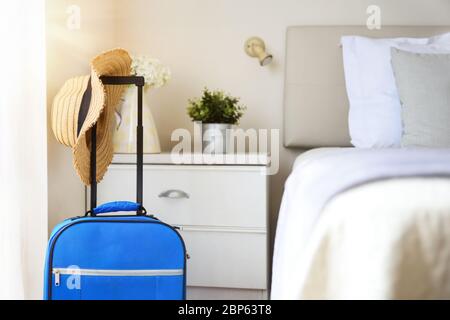 Bright and sunny vacation hotel room with suitcases and straw hat hanging on the bed. Stock Photo