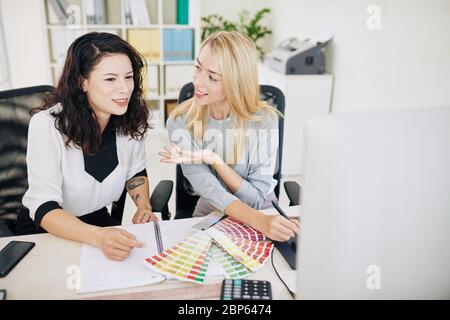 Positive female UX and UI designers sitting at office desk and discussing color scheme for new project Stock Photo