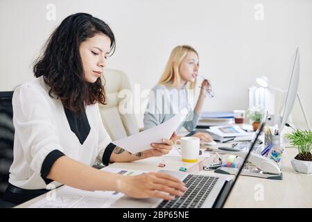 Serious businesswoman reading important document and answering e-mails from clients Stock Photo