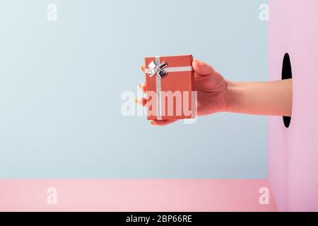 Woman's hand holding a gift box on blue and pink background Stock Photo