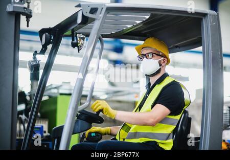 Man worker forklift driver with protective mask working in industrial factory or warehouse. Stock Photo