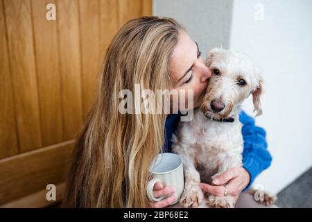 Mature woman relaxing outdoors by front door at home with coffee and pet dog. Stock Photo