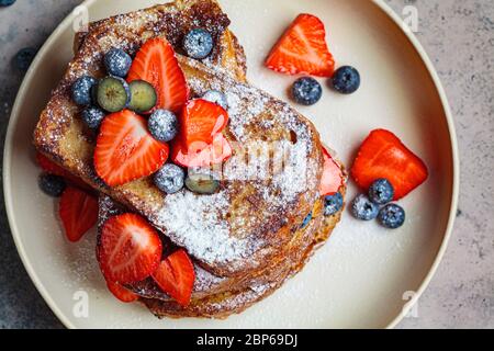 Traditional French toast with blueberries, strawberries and powdered sugar on a white plate. Stock Photo