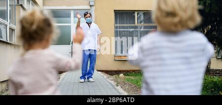 Children greeting father doctor from distance in front of hospital, coronavirus concept. Stock Photo
