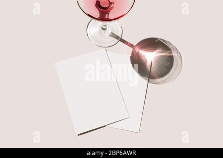 Summer stationery still life scene. Glass of red wine, cocktail, long shadow. Blank greeting cards mockups scene. Pink table background in sunlight. F Stock Photo