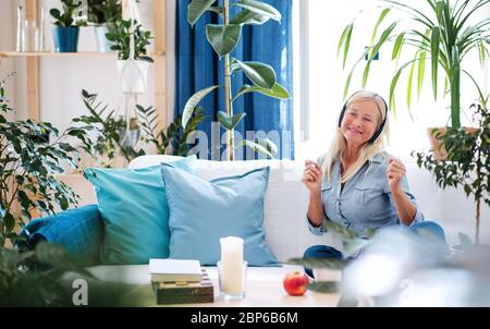 Attractive senior woman with headphones sitting indoors on sofa, relaxing. Stock Photo