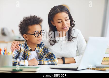 Portrait of cute African boy wearing big glasses while using laptop with mom, homeschooling and remote education concept Stock Photo