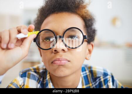 Close up portrait of cute African-American boy wearing big glasses frowning and pouting while doing homework Stock Photo