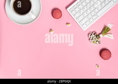 Female workspace with keyboard, cup of black coffee, two macarons and bunch of daisy flowers on pink background from above. Home office, freelance or Stock Photo